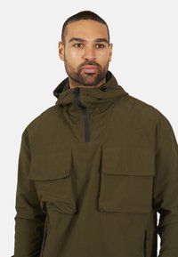 Olijfgroene pulloverjack met een hoge kraag, twee borstzakken en een rits aan de voorkant. Gemaakt van lichtgewicht, gestructureerde stof met een ontspannen pasvorm.