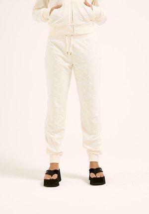 Pantaloni jogger color crema con un motivo testurizzato, dotati di tasche, polsini elasticizzati e vita con cordino. Abbinati a sandali platform neri.