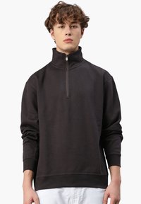 Schwarze Zip-Up Sweatshirt aus weichem Material, mit hohem Kragen, gerippten Bündchen und lockerer Passform. Minimalistisches Design ohne Muster.