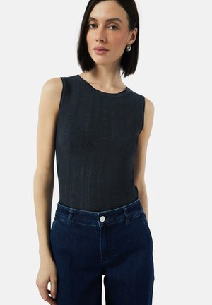 Navy mouwloos topje met een gemêleerd golvenpatroon, gecombineerd met high-waisted donkere denim jeans met een metalen knoop en blauwe stiksels.