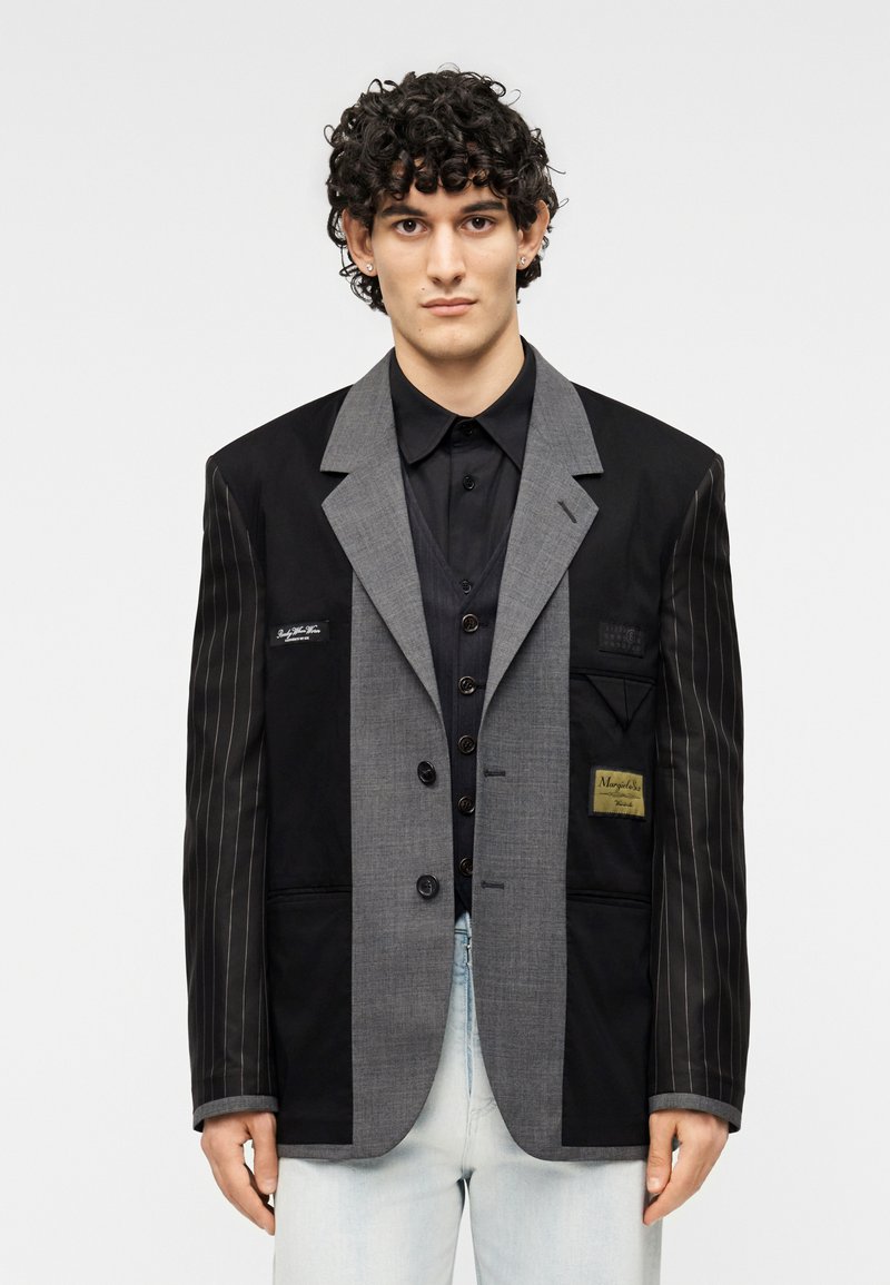Μαύρο και γκρι σακάκι πατςγουορκ με ριγέ και μονές περιοχές, διαθέτει κουμπιά, λεπτομέρειες τσέπης και ετικέτα στο μπροστινό μέρος.