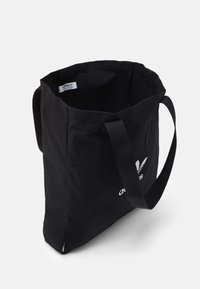 Černá taška Adidas s dlouhými uchy, otevřeným vrchem a bílým logem na přední straně, vyfotografována na bílém pozadí.