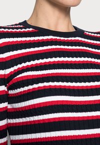 Ribbed knit sweater featuring horizontal stripes in navy, red, and white. Classic round neckline with a textured finish.