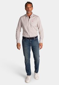 Witte overhemd met knopen en een klein patroon, gecombineerd met blauwe jeans en witte sneakers. Heeft een rood logo op de borst.
