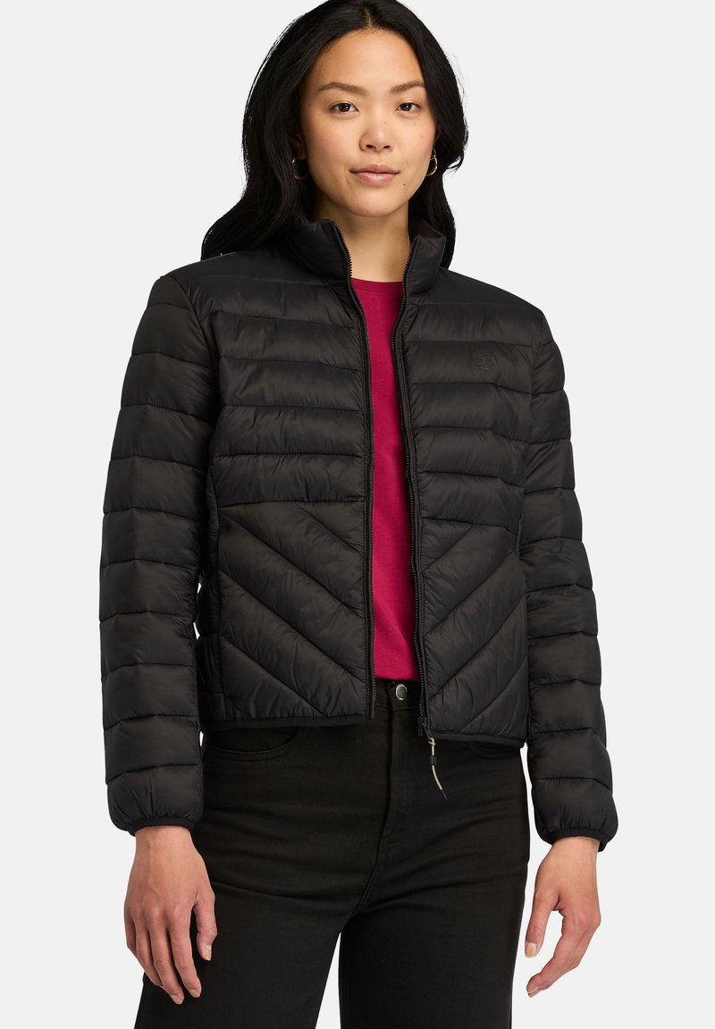 Giubbotto puffer nero con un design leggero, motivo a chevron, chiusura frontale con zip e polsini a costine, abbinato a una maglia rossa.