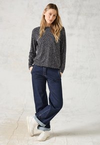 T-shirt à manches longues noir avec un motif de feuilles blanches, associé à un jean droit bleu foncé et des baskets blanches, montrant des poignets retroussés.