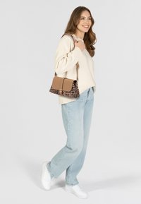 Borsa marrone e a stampa leopardata con tracolla staccabile, forma rettangolare, superfici lisce e testurizzate, indossata con jeans chiari e sneakers bianche.