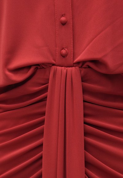 Piros szövetruha sima textúrával, gombos elülső résszel és deréknál összegyűrt ráncokkal a határozottabb sziluettért.