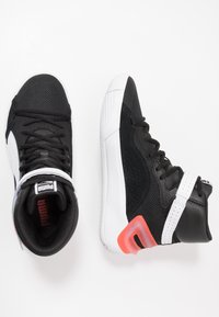 Baskets montantes Puma noir et blanc avec lacets et une touche de rouge sur la semelle, présentées en vues de dessus et de côté sur un fond blanc.