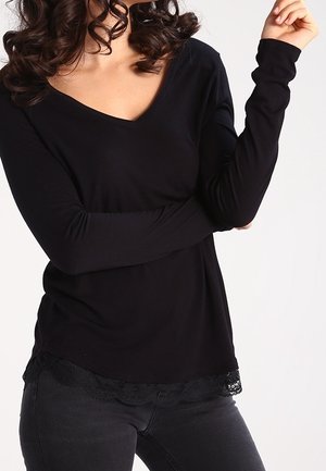 Musta pitkähihainen paita, jossa on V-pääntie ja pitsireunus helmassa, pehmeä rakenne ja rento istuvuus. Yhdistetty tummaan farkkukankaisiin.