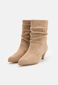 Bottines en daim beige au design décontracté, bout pointu et talon carré de 5 cm. Texture lisse, sans ornements visibles.