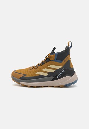 Gheată de drumeție de tip înalt, cu o schemă de culori galben și negru, superior din plasă, talpă din cauciuc și detalii cu trei dungi albe.