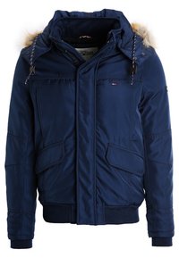 Marinblå vadderad vinterjacka med pälsbeklädd huva, framsida med dragkedja och tryckknappsstängning, fickor med lock samt ribbade manschetter och nederkant.