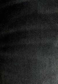 Černá denímová látka s hladkým povrchem, vykazující jemný lesk a diagonální vzor tkaní, což naznačuje kvalitní materiál a zpracování.