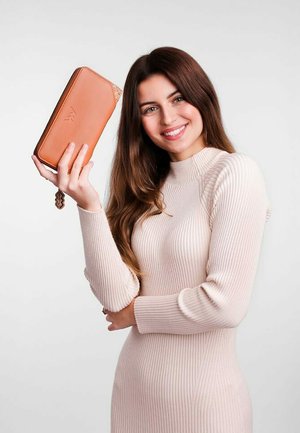 Braune Lederbörse mit strukturiertem Design, rechteckiger Form und Handgelenkband. Modell hält sie vor einem schlichten Hintergrund.