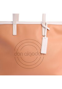Bolso tote de cuero durazno con acentos blancos, que presenta un diseño circular perforado y etiqueta de la marca. Textura suave, dos asas.
