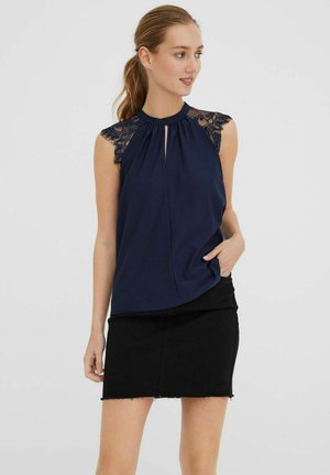 Tamsiai mėlynas be rankovių topas su nėriniuotomis pečių dalimis, raktų angos priekyje, minkšta medžiaga, derinama su juoda džinsine mini sijonu.