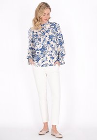 Blusa floreale in crema e blu con maniche lunghe e a sbuffo; abbinata a pantaloni bianchi slim e ballerine color beige chiaro.