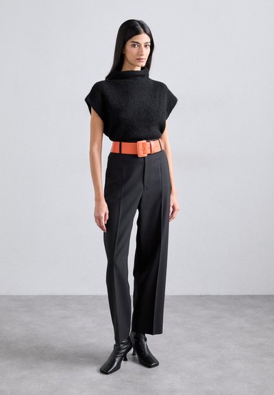 Maglietta nera a maniche corte in maglia abbinata a pantaloni neri a vita alta e una cintura in pelle arancione. Il modello indossa stivaletti neri opachi con tacco.