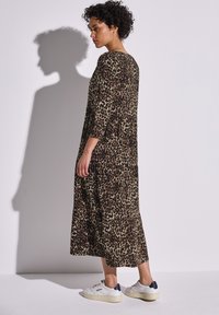 Vestido de manga larga con estampado de leopardo en tonos marrón y beige. Corte holgado y a la altura de la rodilla, combinado con zapatillas blancas. Tejido texturizado.