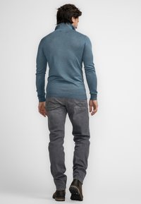 Turfkleurige polo met lange mouwen en hoge kraag, geribde manchetten en zoom, gecombineerd met grijze jeans en donkere laarzen. Soepele textuur, casual pasvorm.