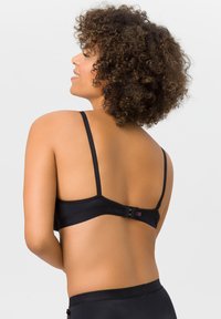 Black bra with thin adjustable straps, a smooth texture, and a hook-and-eye closure at the back. Features a subtle logo detail on the band.