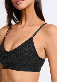 Czarny top typu bralette o teksturowanej powierzchni, z metaliczną nitką, trójkątnymi miseczkami, regulowanymi ramiączkami i szerokim pasem na dole.