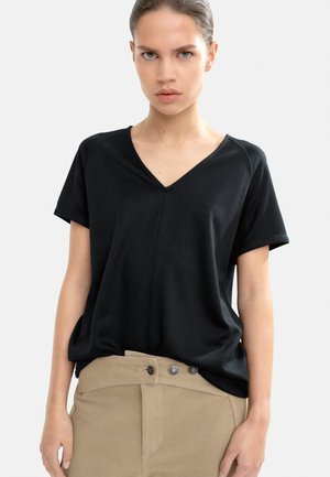 Black short-sleeve V-neck top made of soft fabric, featuring a subtle seam detail at the front and a relaxed fit, paired with tan high-waisted pants.