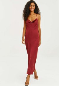 Hedvábná šaty s kapucí v hlbokom burgundskom odtieni, prezentujúce úzke ramienka a priliehavý strih, ktorý sa splýva až na zem s minimálnym zdobením.