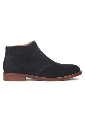 Bottine en cuir suédé noir avec semelle marron et petit talon, dotée d'une fermeture à lacets et de détails de couture soignés.