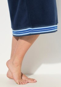Robe in fleece blu navy con un orlo caratterizzato da strisce blu chiaro e blu scuro. Primo piano di piedi nudi e pelle texturizzata vicino all'orlo.