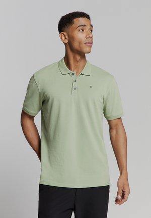Hellgrünes Poloshirt aus strukturiertem Baumwollstoff, mit klassischem Kragen, drei Knöpfen und einem kleinen Logo auf der Brust.