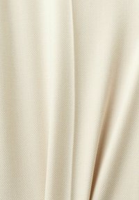 Tissu beige texturé avec un motif tissé subtil, présentant de doux plis créant un drapé élégant. Idéal pour les vêtements ou la tapisserie.