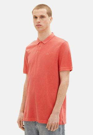 Korallenfarbenes Poloshirt mit klassischem Kragen, zwei Knopfverschluss und kleinem Logo-Akzent. Der Stoff wirkt weich mit einer lockeren Passform und kurzen Ärmeln.