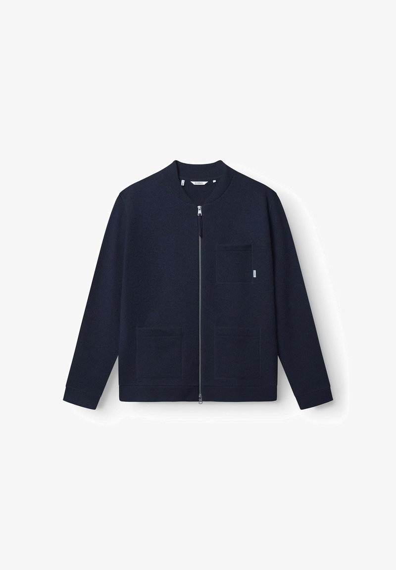 Veste zippée bleu marine en tissu texturé, présentant un col rond, deux poches avant et des détails de design minimalistes.