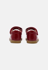 Scarpe rosse in vernice con punta arrotondata, cinturino alla caviglia e suola in gomma beige. Tessuto liscio con finitura lucida e senza decorazioni visibili.