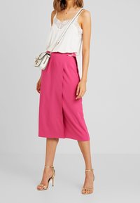 Witte cami met kant, gecombineerd met een levendig roze culotte, met een strak ontwerp en soepele stof. Gouden haksandalen en een witte tas maken de look compleet.