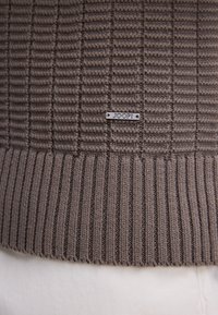 Sweter dzianinowy w ziemistym brązie, z teksturowanymi pionowymi paskami i ściągaczem u dołu. Zawiera metalową metkę z logo "JOOP!"