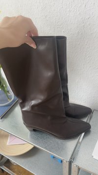 Bruna knähöga stövlar i slätt syntetmaterial, med spetsig tå och en avslappnad design. Minimalistisk stil utan synlig hårdvara.