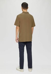 Braunes Poloshirt mit kurzen Ärmeln, Rückansicht, kombiniert mit marineblauen Cargohosen und weißen Sneakern. Einfaches Design, reguläre Passform, keine sichtbaren Muster.