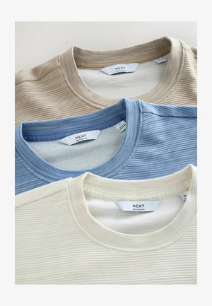 Trzy t-shirty o luźnym kroju z okrągłym dekoltem w kolorze beżowym, jasnoniebieskim i kremowym, z wypukłą fakturą i widocznymi etykietami na dekolcie.