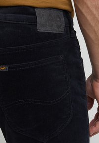 Marina kordfløyelsbyxor har ett texturerat tyg, synliga sömmar och en läderlapp med texten "Lee" vid midjan.