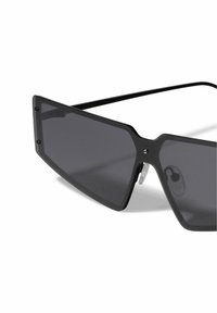 Black oversized sunglasses with angular frame, gray tinted lenses, and transparent nose pads. Features metal accents near the lenses.