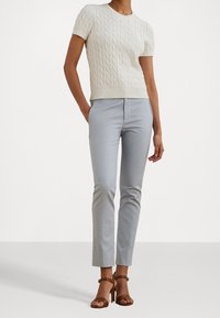 Weißer, kabelgestrickter Pullover mit kurzen Ärmeln, kombiniert mit hellgrauen, taillierten Hosen und braunen, gestriegen High Heels. Einfaches und elegantes Design.