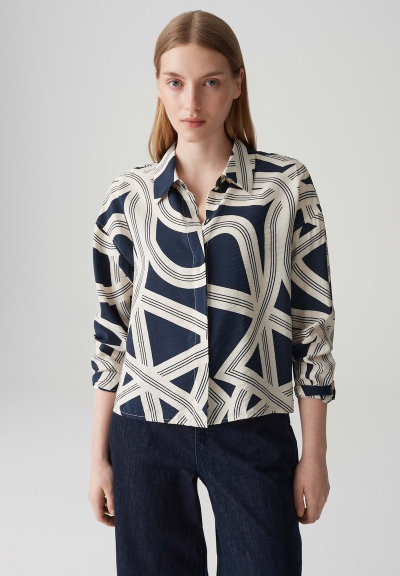 Blusaa navy e crema con pattern a linee astratte, colletto a bottoni, maniche lunghe e taglio morbido. Realizzata in un tessuto leggero.