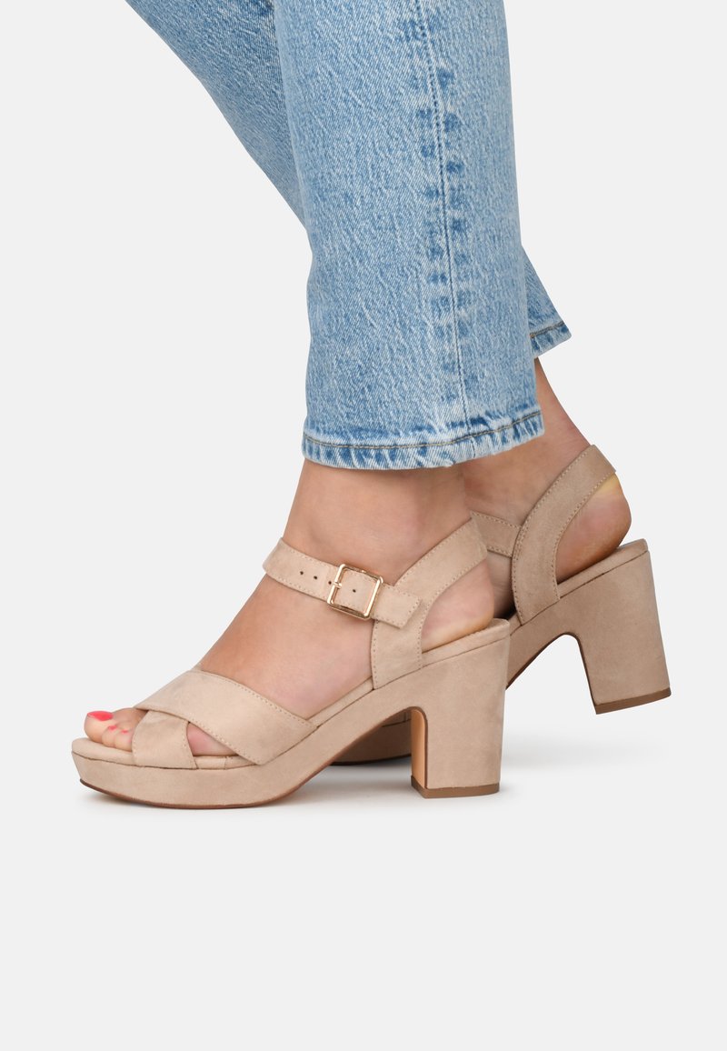 Beige suède sandalen met blokhak, kruisbanden en een verstelbare gesp. Voorzien van een textuurafwerking en een open hielontwerp.