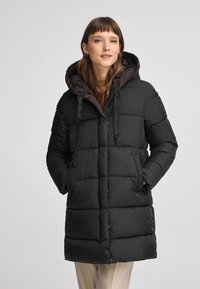 Czarna kurtka puchowa z pikowanym wzorem, brązowym kapturem, detalami ze sznurkiem oraz bocznymi kieszeniami dla funkcjonalności i ciepła.