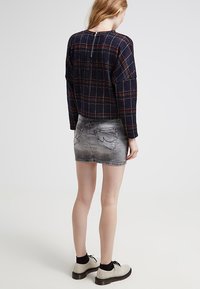 Námořnický kostičkovaný zkrácený svetr se zipem na zádech, doplněný o vybledlou šedou džínsovou sukni s dvěma zadními kapsami. Nosený s béžovými botami.