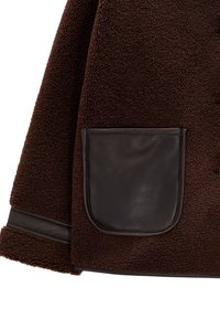 Brązowa kurtka z polaru o teksturowanej powierzchni, z ciemną skórzaną kieszenią i wykończeniem wzdłuż dolnego brzegu.