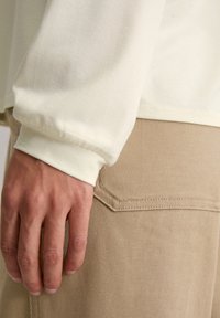 Lange mouw crèmekleurig shirt met geplooide manchetten, gecombineerd met beige corduroy broeken met een gebogen achterzak en een gestructureerde stof.